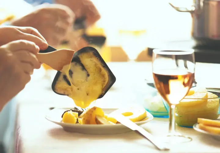 Raclette fondue dégoulinant sur des pommes de terre, un verre de Bourgogne Aligoté à côté.
