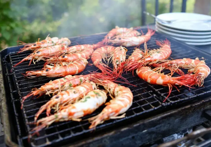 Grosses gambas barbecue sur un grill, fumant et appétissant. Les crevettes sont bien caramélisées, prêtes à être dégustées.