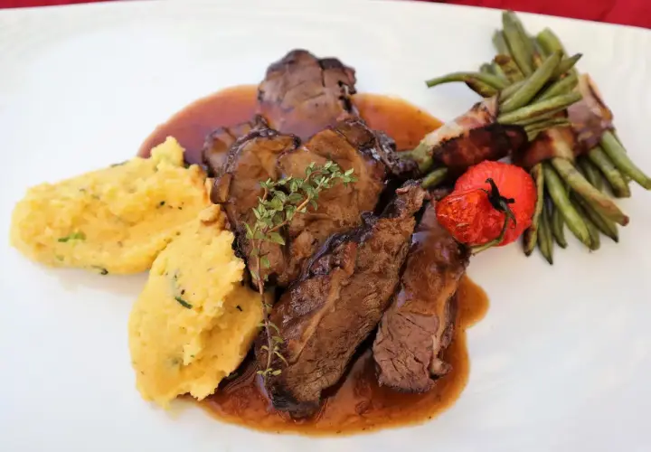 Savoureux sabodet au vin rouge, servi avec une polenta crémeuse, des haricots verts enroulés de lard et une tomate confite.