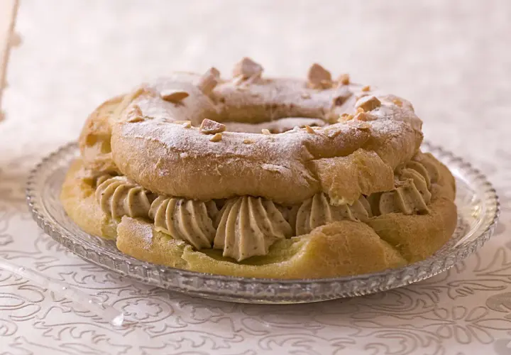 Un Paris-Brest garni d'une généreuse crème mousseline praliné, saupoudré de sucre glace et d'éclats de noisettes.