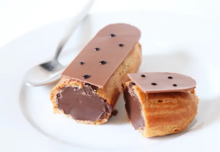 Deux éclairs au chocolat, un entier et un coupé, sur une assiette blanche avec une cuillère. Parfait pour une recette éclair au chocolat.