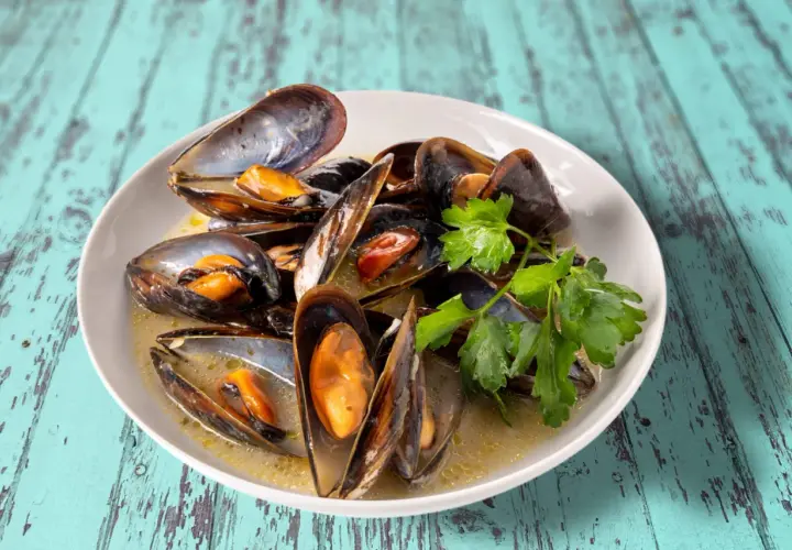 Un plat de moules au roquefort, garni de persil frais, baignant dans une sauce crémeuse. Un délice savoureux sur une table en bois bleu délavé.