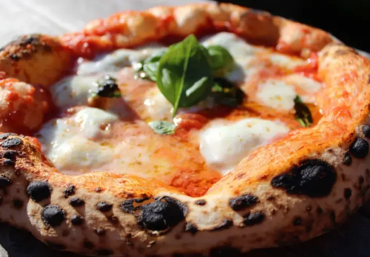 Une pizza napolitaine authentique, avec sa croûte gonflée et tachetée, garnie de sauce tomate, mozzarella fondante et basilic frais. La recette parfaite pour un délice italien.