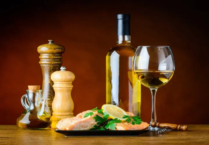 Un plat de saumon avec citron et persil, accompagné d'une bouteille et d'un verre de bon vin blanc sec, d'une salière, d'une poivrière et d'une burette d'huile d'olive.