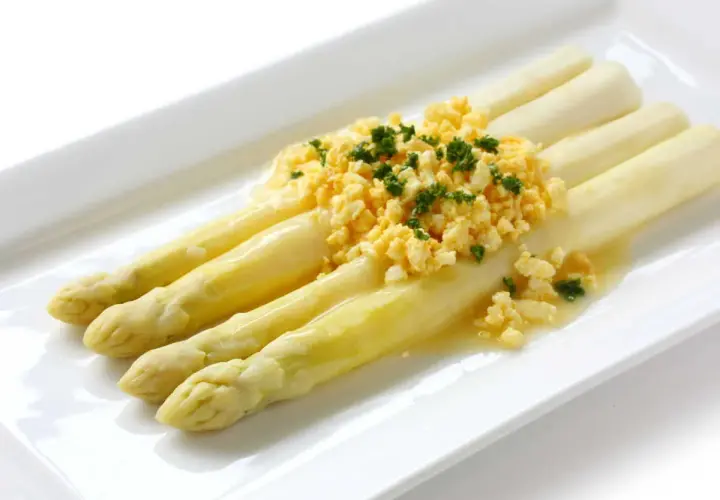 Asperges à la flamande : des asperges blanches tendres nappées d'une sauce savoureuse et garnies d'œufs brouillés et de persil frais.
