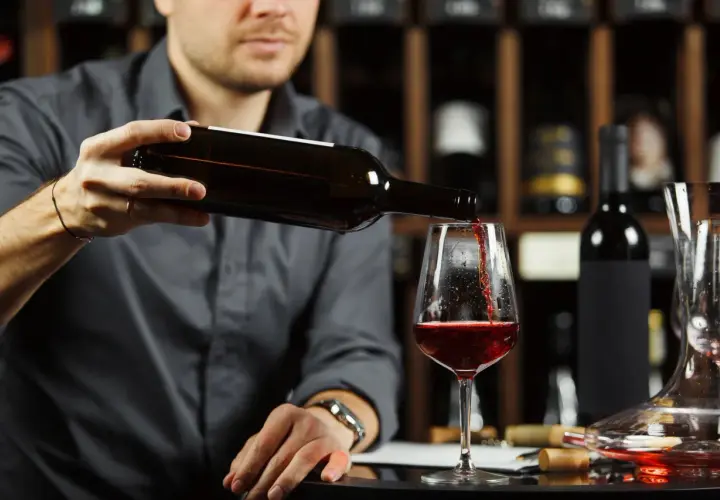 Un homme verse un vin rouge profond dans un verre, une cave à vin en arrière-plan. Quel vin rouge savoureux !