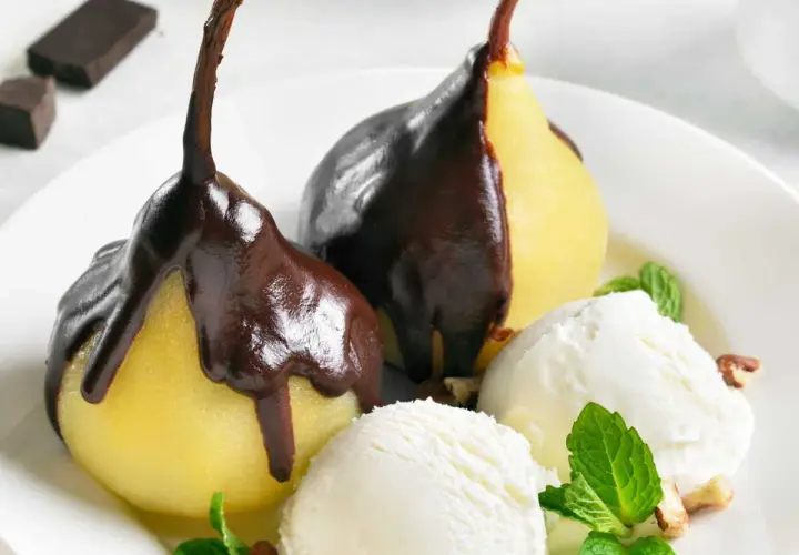 Poires pochées nappées de chocolat noir, servies avec de la glace à la vanille et des éclats de noisettes. Un délice de poire Belle Hélène.