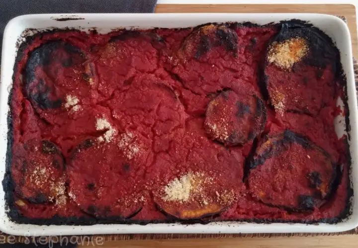 Un plat de parmigiana di melanzane tout juste sorti du four, avec des bords légèrement caramélisés et une sauce tomate savoureuse.