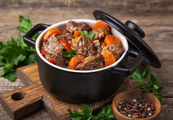 Un délicieux bœuf bourguignon mijoté dans une cocotte minute SEB, garni de carottes et de persil frais. Un plat réconfortant prêt à être dégusté.