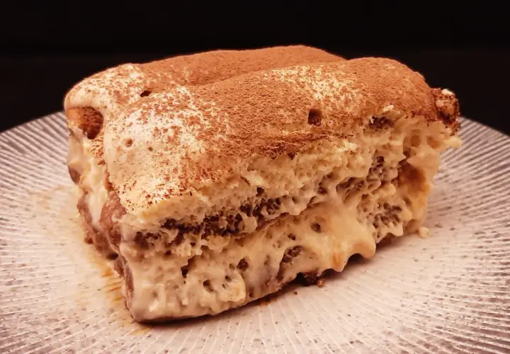 Un généreux tiramisu au café, saupoudré de cacao, repose sur une assiette striée.