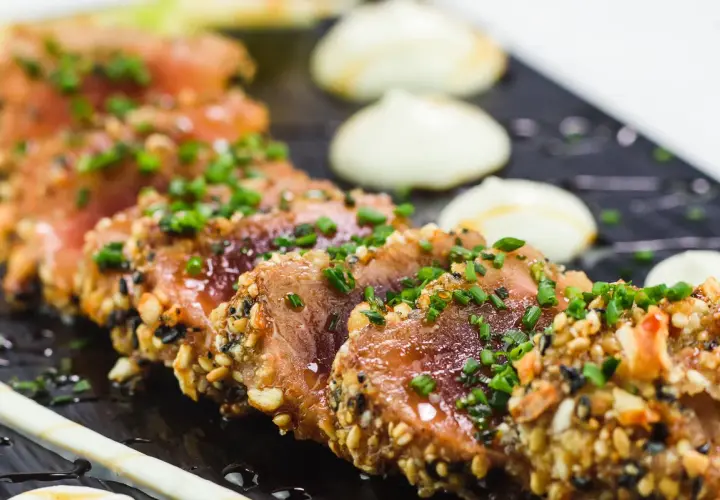 Tataki de thon en croûte de sésame et noix, garni de ciboule fraîche. Un accompagnement visuellement appétissant.