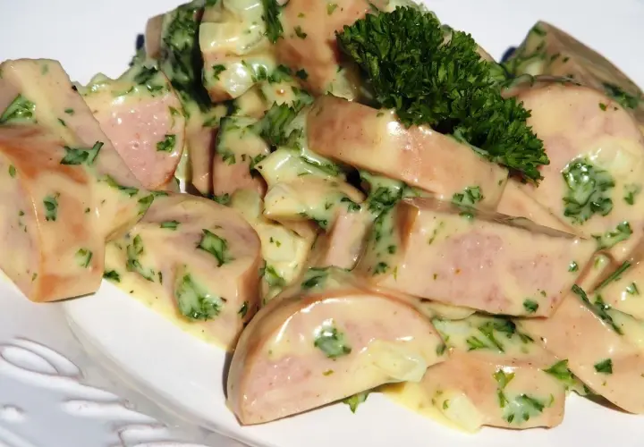 Une délicieuse salade de cervelas, coupée en dés et nappée d'une sauce crémeuse aux herbes fraîches, garnie d'une touche de persil.