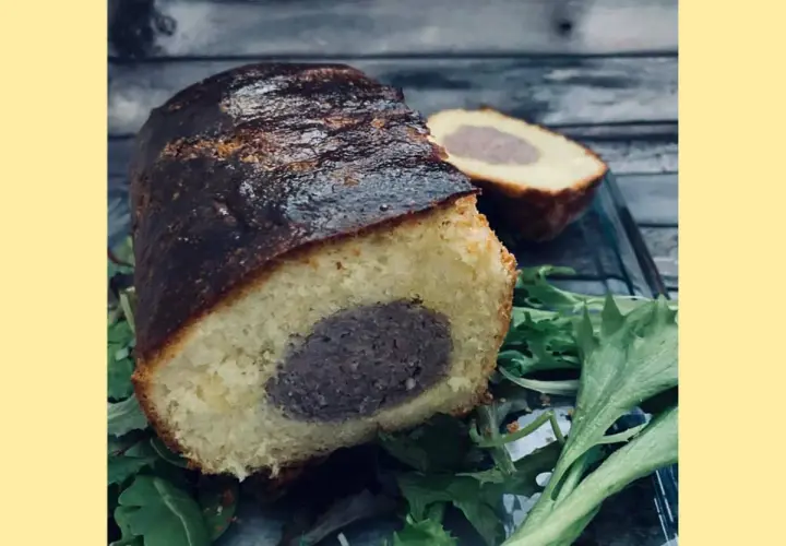 Un délicieux saucisson brioché, coupé en deux, repose sur un lit de verdure. Sa croûte dorée et sa mie moelleuse invitent à la dégustation.