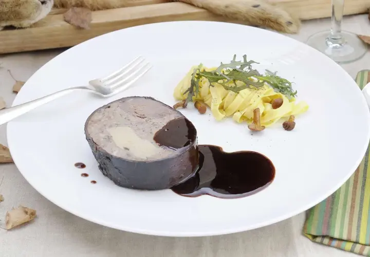 Un rôti de lièvre à la royale, garni de foie gras, servi avec des pâtes fraîches, des champignons et une sauce au vin.