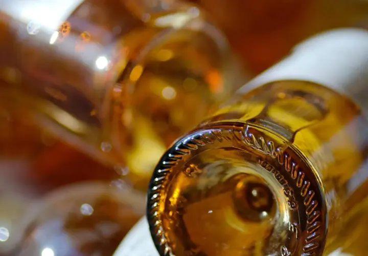 Gros plan sur le goulot d'une bouteille de vin ambré, évoquant un sauterne sec ou moelleux. Reflets lumineux sur le verre.