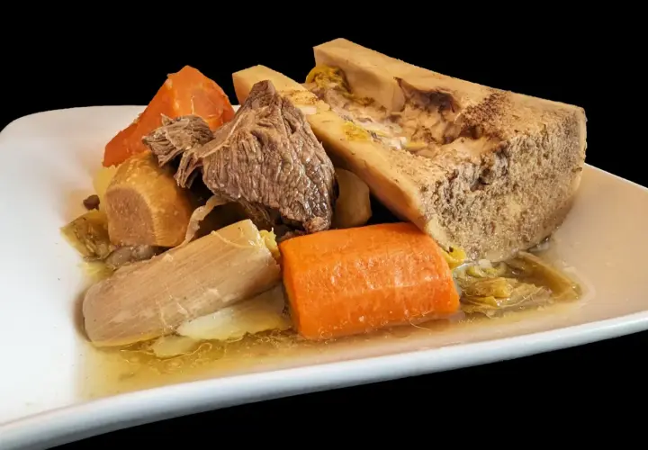 Un plat généreux de pot-au-feu cocotte minute : viande, os à moelle, carottes et poireaux mijotés dans un bouillon savoureux.