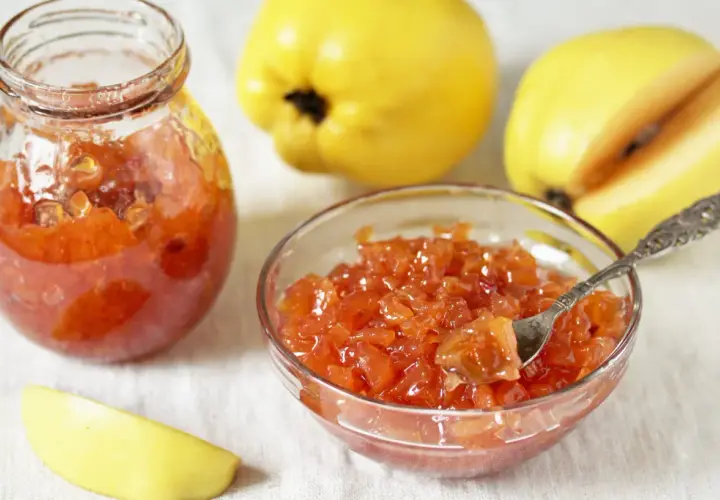 Confiture de coings sans les peler, servie dans un bocal et un bol, avec des coings entiers et une tranche en arrière-plan.