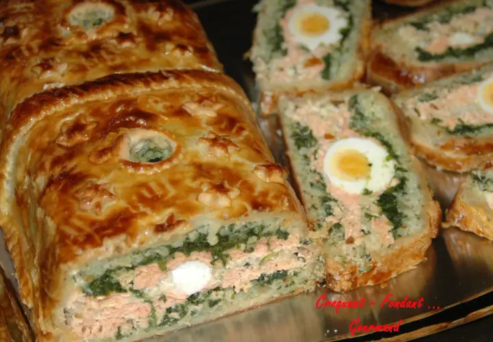 Un koulibiac de saumon doré, garni d'épinards et d'œufs durs, est coupé en tranches appétissantes.