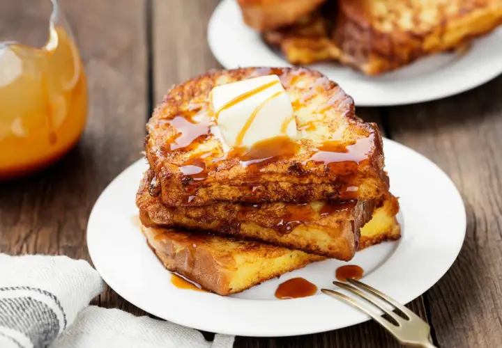 Pile de pain perdu doré, nappé de sirop et garni de beurre fondant. Un délice matinal.