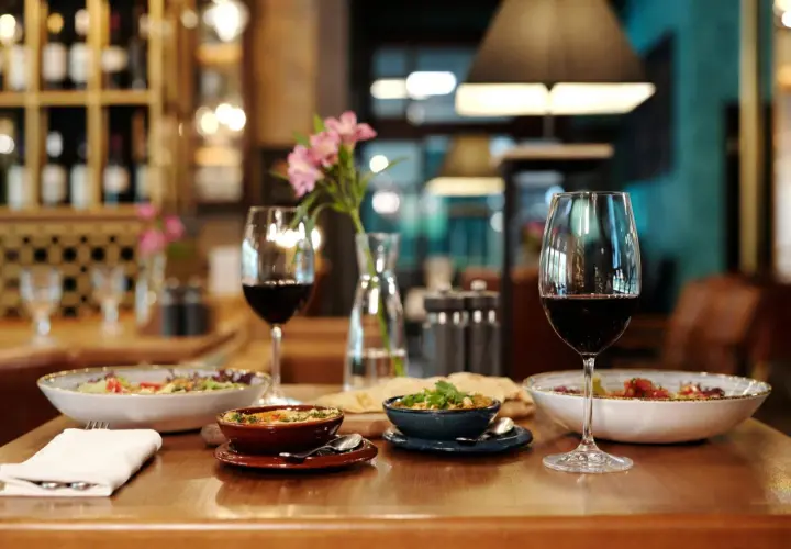 Verre de vin rouge tannique et puissant, accompagné de plats appétissants et d'une touche florale, dans une ambiance de restaurant chaleureuse.