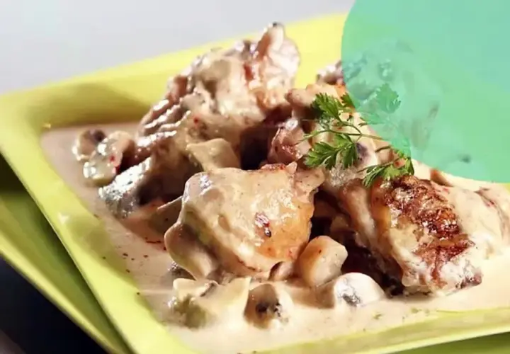 Un plat de fricassée de volaille crémeuse avec des champignons, garni de persil frais, servi dans une assiette jaune vif.