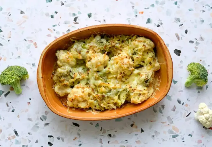 Un délicieux gratin chou-fleur brocolis, gratiné au fromage, servi dans un plat en terre cuite. Quelques fleurons frais entourent le plat.
