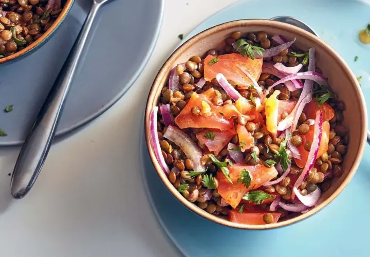 Salade de lentilles savoureuse avec du saumon fumé, des tomates et des oignons rouges, garnie de persil frais.