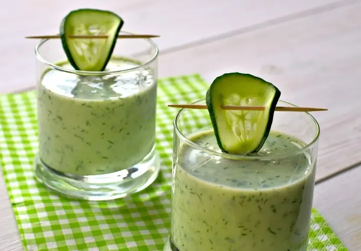 Deux verres de gaspacho concombre, décorés d'une tranche de concombre sur un cure-dent, sur une nappe à carreaux verts.