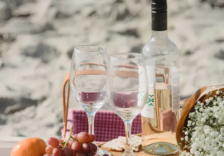 Un pique-nique sur la plage avec des verres, des raisins et une bouteille de vin. Idéal pour savoir comment choisir un vin rosé parfait pour l'occasion.