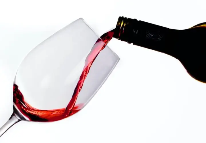 Le vin rouge, fruit d'une macération soignée, coule d'une bouteille dans un verre.