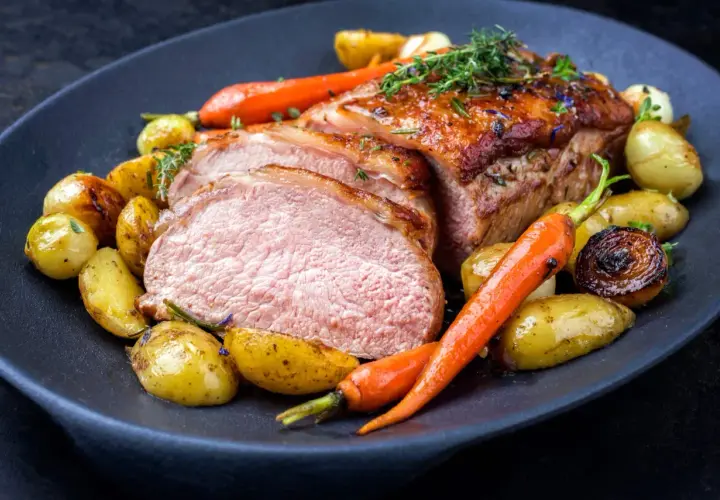 Délicieuse côte de veau barbecue, tranchée et servie avec des pommes de terre rôties et des carottes glacées, garnie d'herbes fraîches.