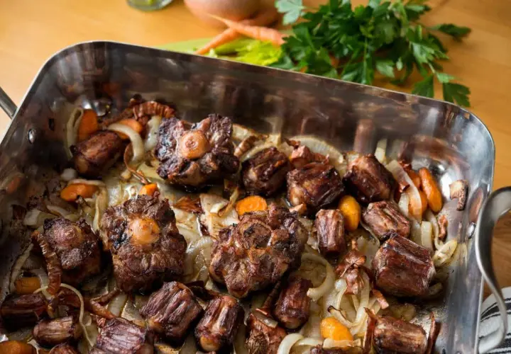 Morceaux de queue de bœuf rôtis dans un plat avec des oignons et des carottes. Un plat savoureux, parfait pour un fond de veau riche.