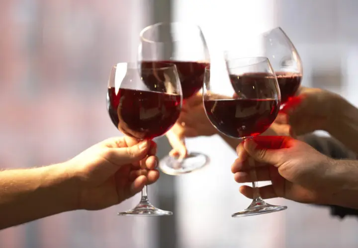 Quatre mains portent des verres de vin rouge pour un toast. Une belle façon de célébrer et de savoir comment boire du vin rouge.