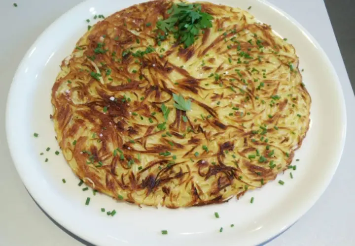Une pomme darphin dorée et croustillante, garnie de ciboulette fraîche et de persil, servie sur une assiette blanche.
