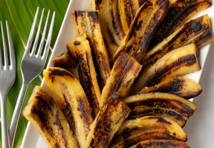 Bananes flambées grillées sur une feuille de bananier, prêtes à être dégustées avec deux fourchettes.