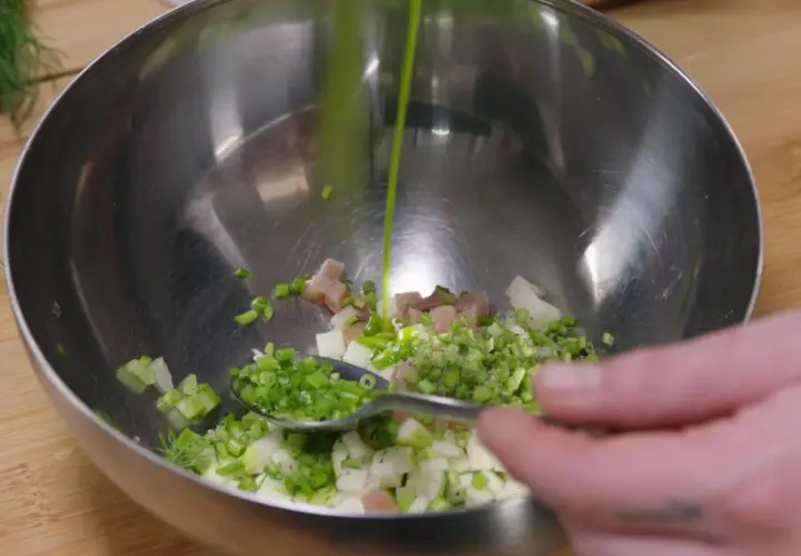 Préparation d'une salade nordique : on verse une sauce verte sur des dés de poisson, oignons et aneth dans un bol.