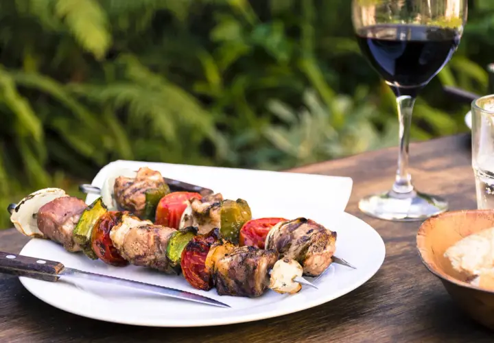 Brochettes de viande et légumes grillés, accompagnées d'un verre de vin pour grillade et d'un bol de pain.