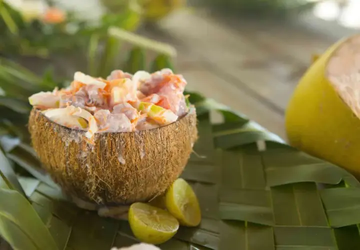 Salade tahitienne crémeuse servie dans une noix de coco, garnie de citron vert et de feuilles de palmier.