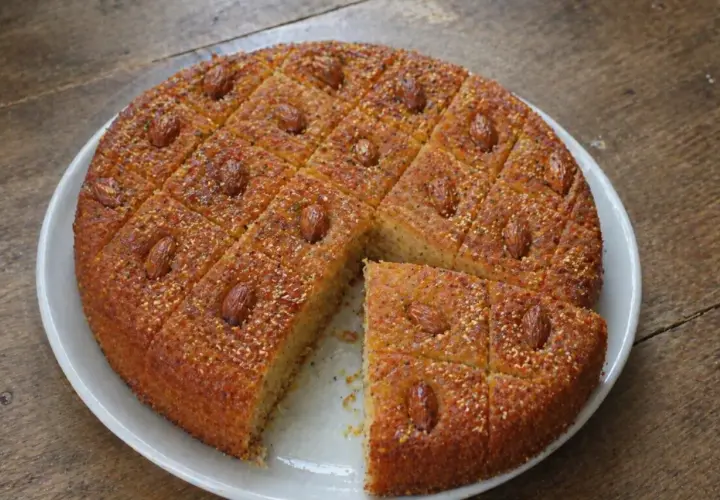 Un délicieux gâteau arabe au miel, parsemé d'amandes et de graines, coupé en carrés sur une assiette blanche.