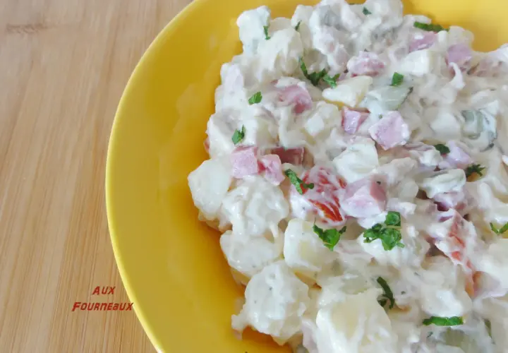 Salade piémontaise maison crémeuse, avec pommes de terre, jambon, tomates et persil, servie dans un plat jaune vif.