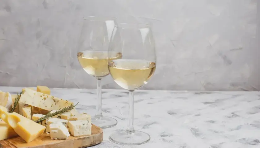 Deux verres de vin blanc pétillant, accompagnés d'une sélection de fromages sur une planche en bois.