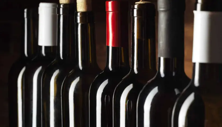 Une rangée de bouteilles de vin rouge, certaines avec des capsules de différentes couleurs, pour vous aider à comment reconnaître un bon vin rouge.