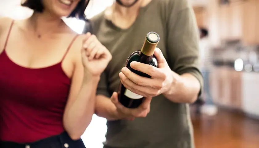 Un couple souriant admire une bouteille de vin rouge, prêt à partager un moment spécial.