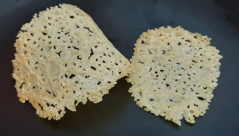 Deux tuiles de parmesan croustillantes et ajourées, posées sur une surface sombre.