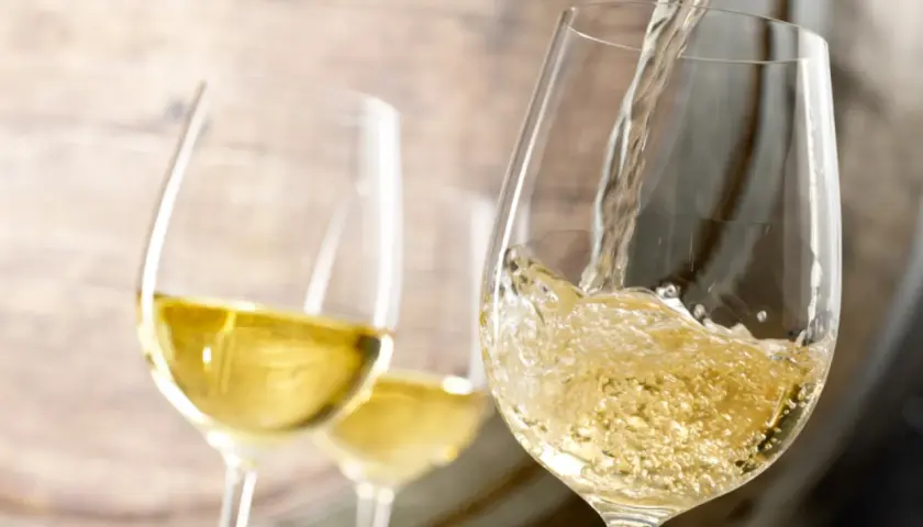 Le vin blanc est versé dans un verre, rappelant le processus de vinification. Deux autres verres sont visibles en arrière-plan.