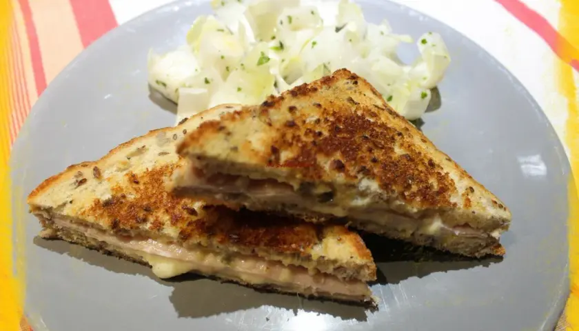 Un délicieux croque monsieur à la poêle, doré et garni de jambon et fromage fondant, servi avec une salade fraîche.
