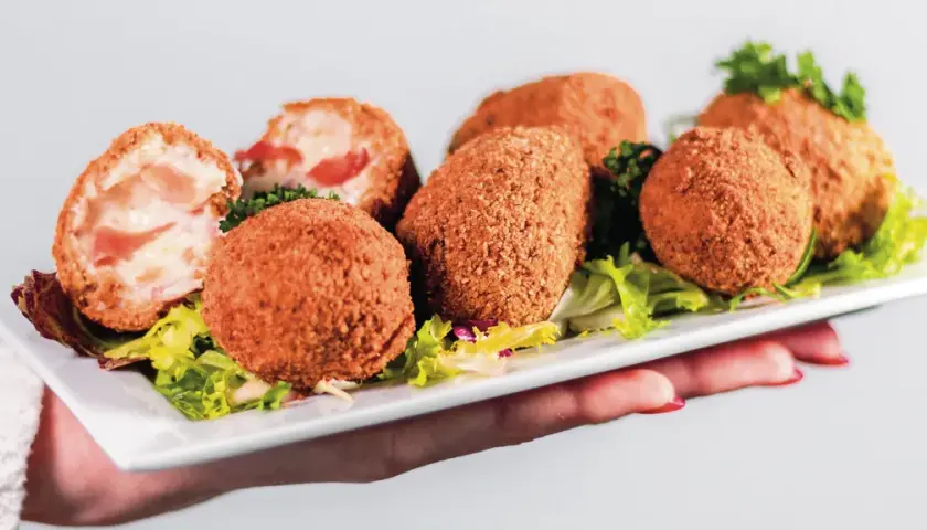 Assiette de croquetas de jambon dorées et croustillantes, garnie de salade verte.