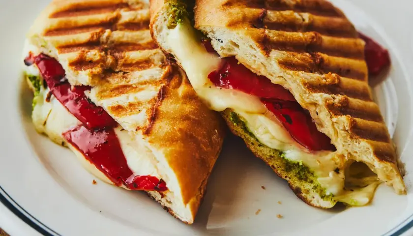 Un délicieux sandwich italien grillé, garni de fromage fondant, de poivrons rouges et de pesto vert.