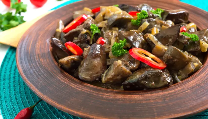 Un plat appétissant de foie de volaille mijoté avec des oignons et garni de persil frais et de rondelles de piment rouge.