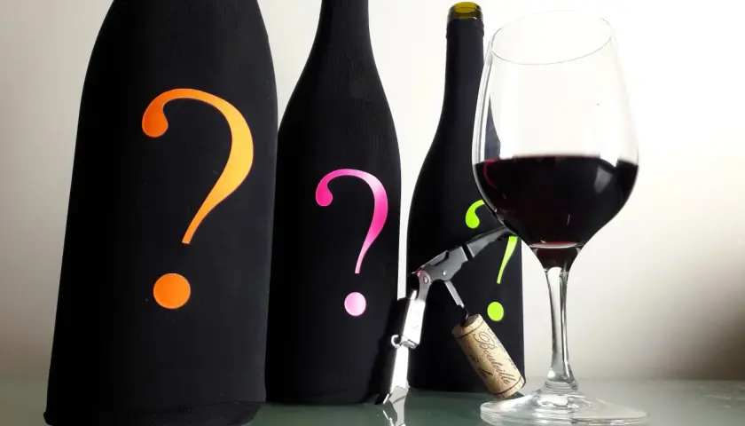 Trois bouteilles mystérieuses, ornées de points d'interrogation colorés, attendent leur dégustation. Un verre de Bourgogne rouge est prêt, suggérant un temps de garde prometteur.